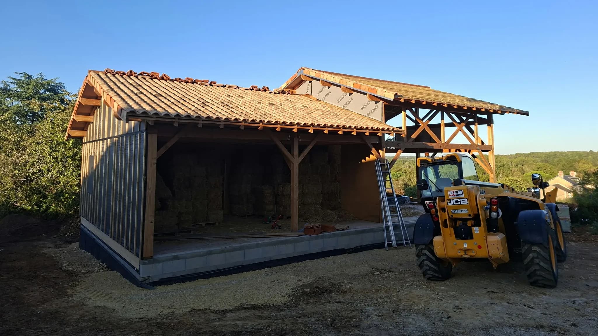 La même construction en chantier : ossature bois, murs en bottes de paille, toiture en cours de couverture