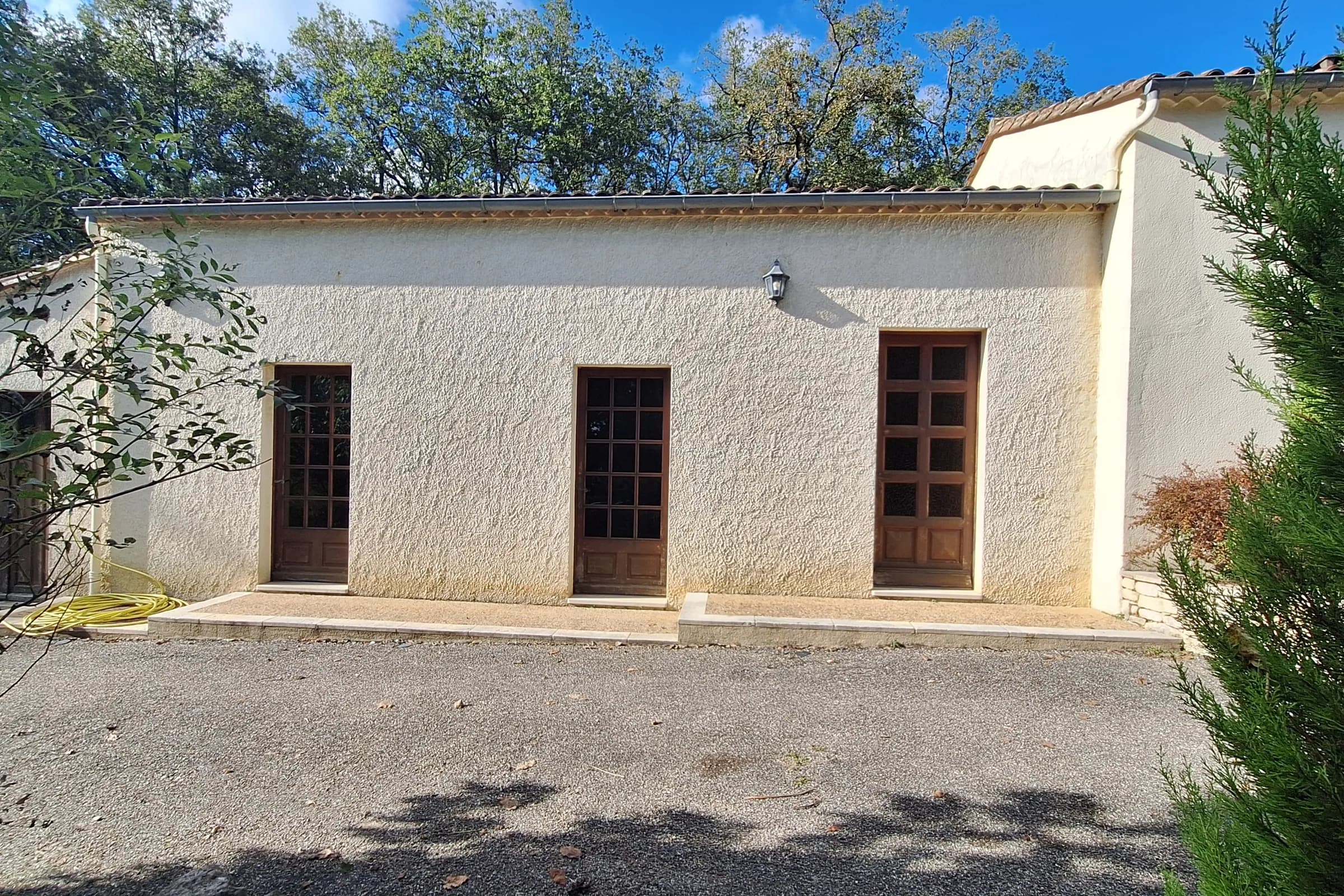 Façade enduite percée de trois portes-fenêtres en bois, avant travaux